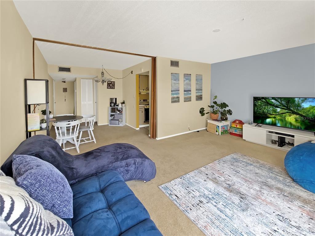 A living room with beige carpet, a blue sectional sofa, and a television on a stand — 2763 WOODGATE LANE UNIT 307, SARASOTA, FL