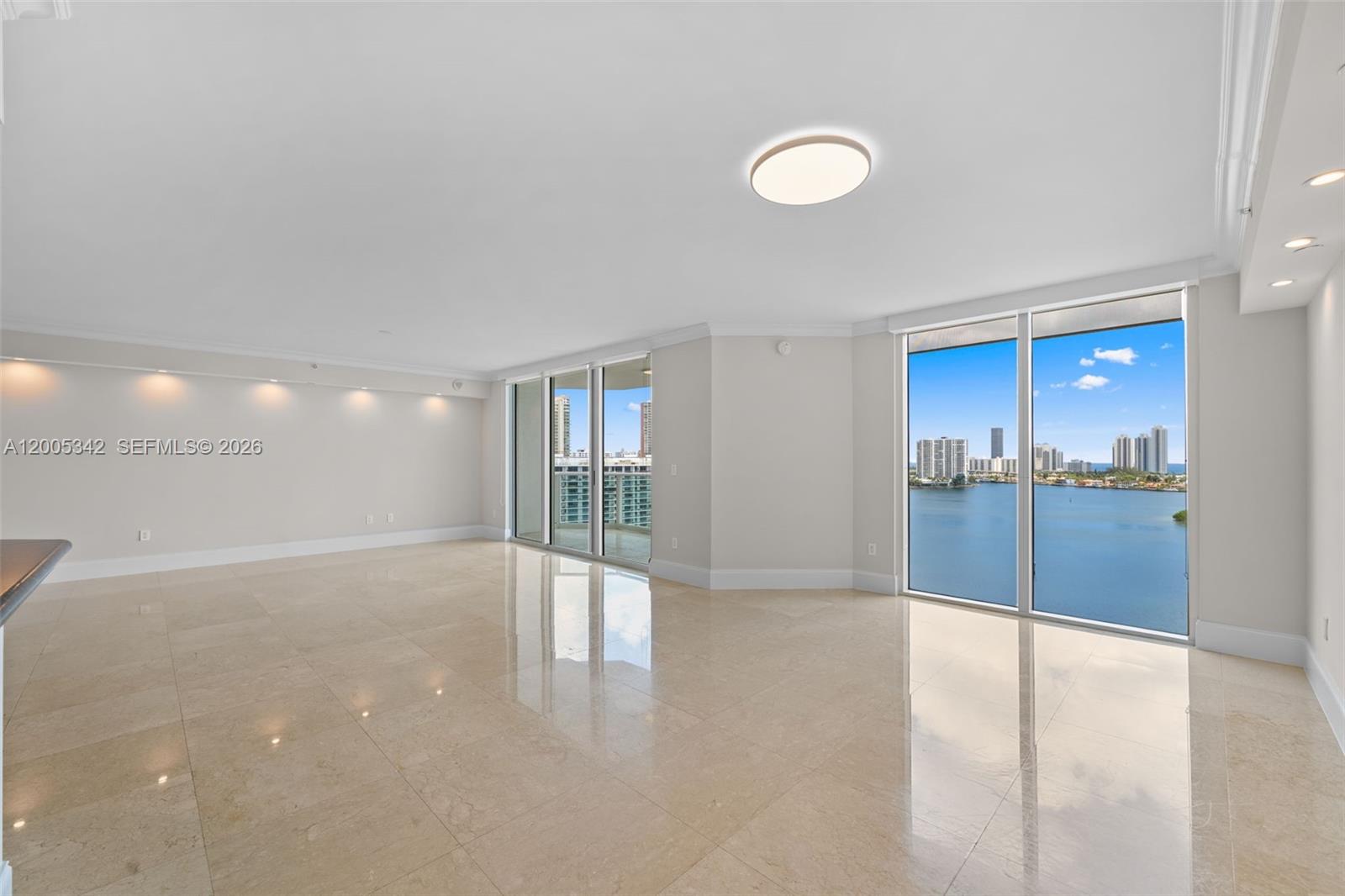 An empty living room features beige tile floors, recessed lighting, and floor-to-ceiling windows overlooking water — 3301 NE 183rd St # 1604, Aventura FL 33160, AVENTURA, FL
