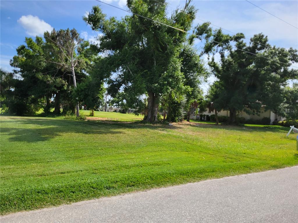 A grassy vacant lot features several large trees and borders a paved road — 68 LONG MEADOW PLACE, ROTONDA WEST, FL
