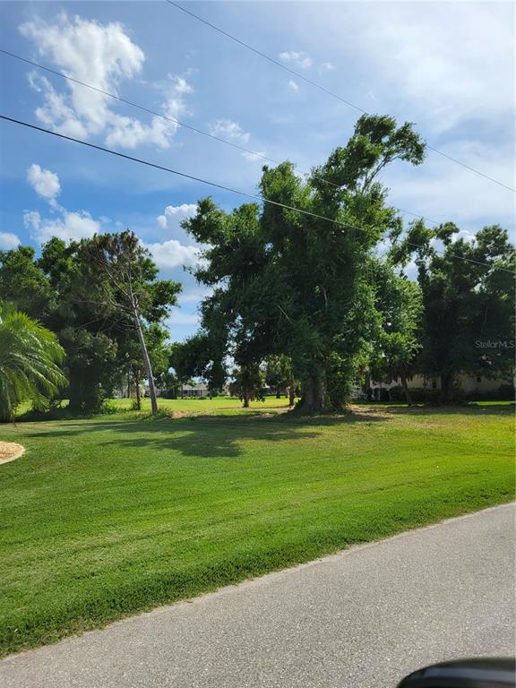 A grassy, vacant lot features several large trees under a blue sky with scattered clouds — 68 LONG MEADOW PLACE, ROTONDA WEST, FL