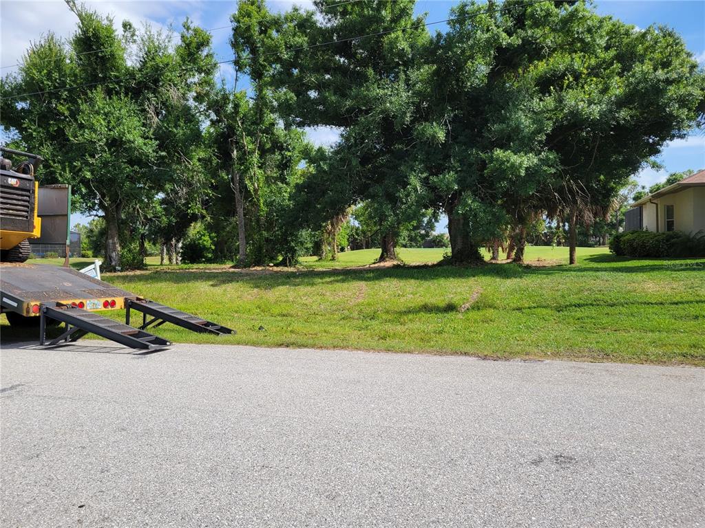 A flat, grassy vacant lot features several large trees and a parked construction trailer — 68 LONG MEADOW PLACE, ROTONDA WEST, FL