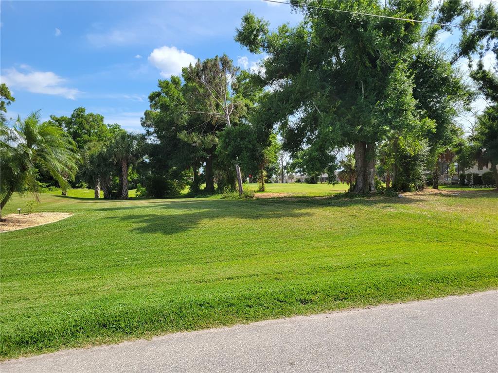 A grassy vacant lot features mature trees and borders a golf course — 68 LONG MEADOW PLACE, ROTONDA WEST, FL