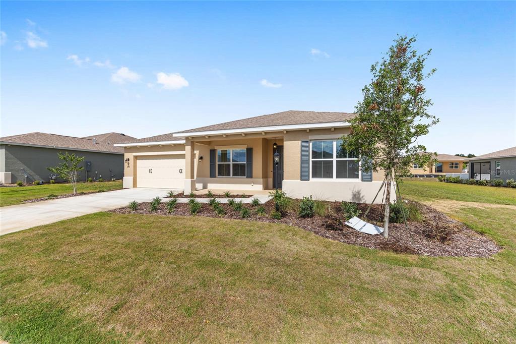 A single-story house with a tan stucco exterior, a two-car garage, and a front lawn — 10313 SW 106TH COURT, OCALA, FL