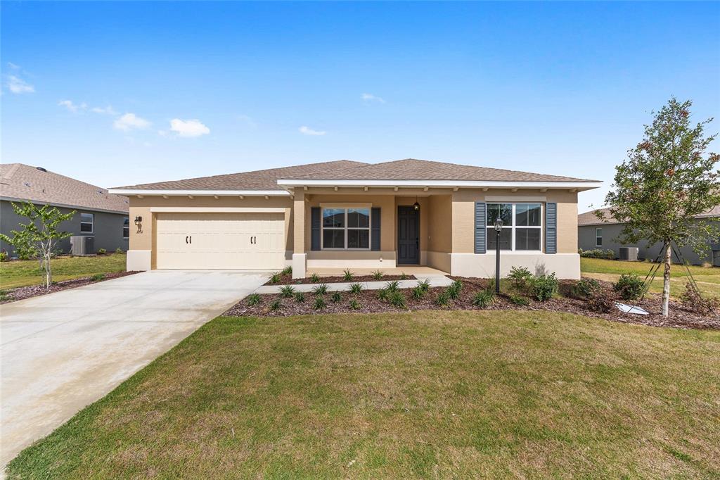 A single-story tan house features a two-car garage, a covered entryway, and blue shutters — 10313 SW 106TH COURT, OCALA, FL