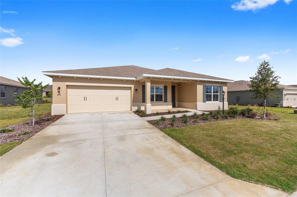 A single-story tan house features a two-car garage, a covered entryway, and a concrete driveway — 10313 SW 106TH COURT, OCALA, FL