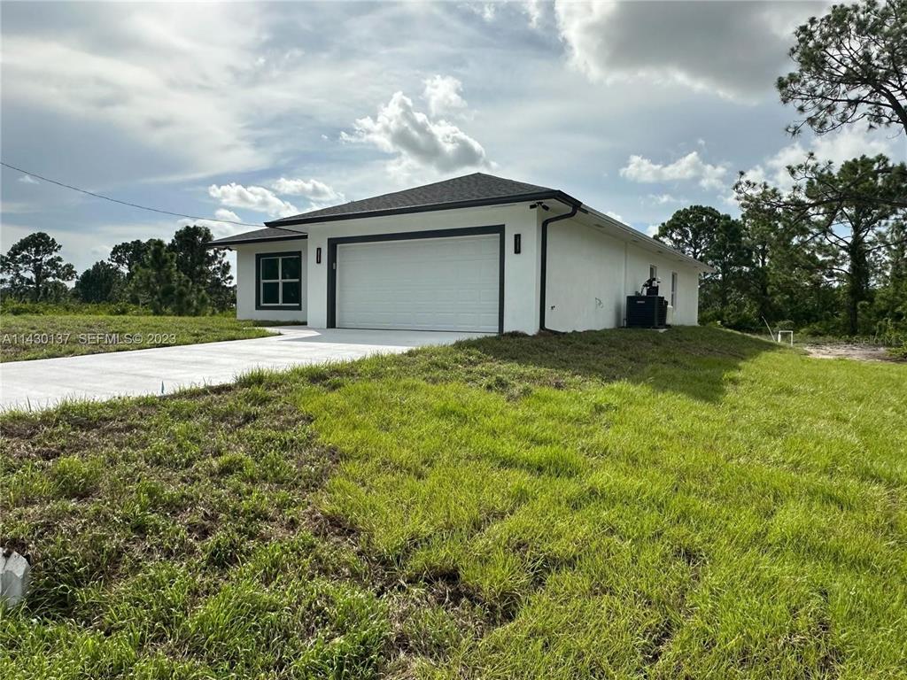 A white, single-story house with a two-car garage sits on a grassy lot — 1125 MILWAUKEE BOULEVARD, LEHIGH ACRES, FL