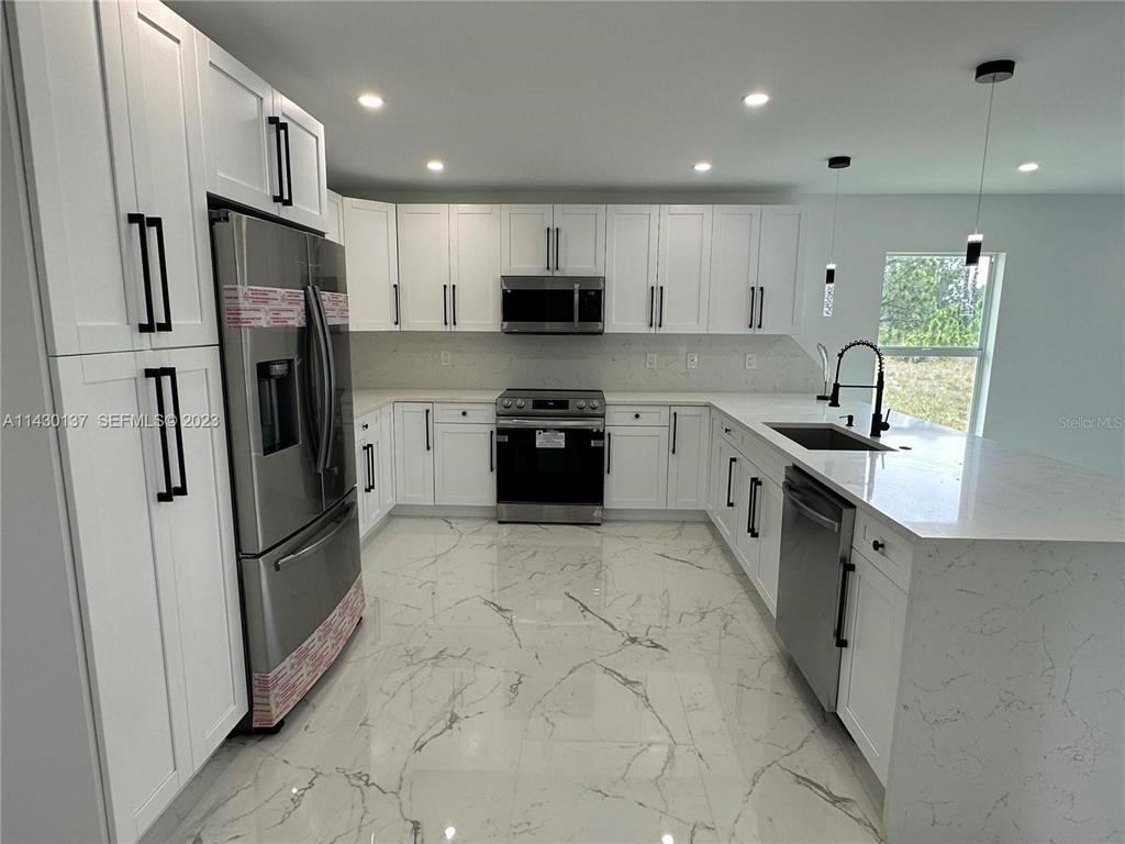 A modern kitchen features white cabinets, stainless steel appliances, and white marble-patterned tile flooring — 1125 MILWAUKEE BOULEVARD, LEHIGH ACRES, FL