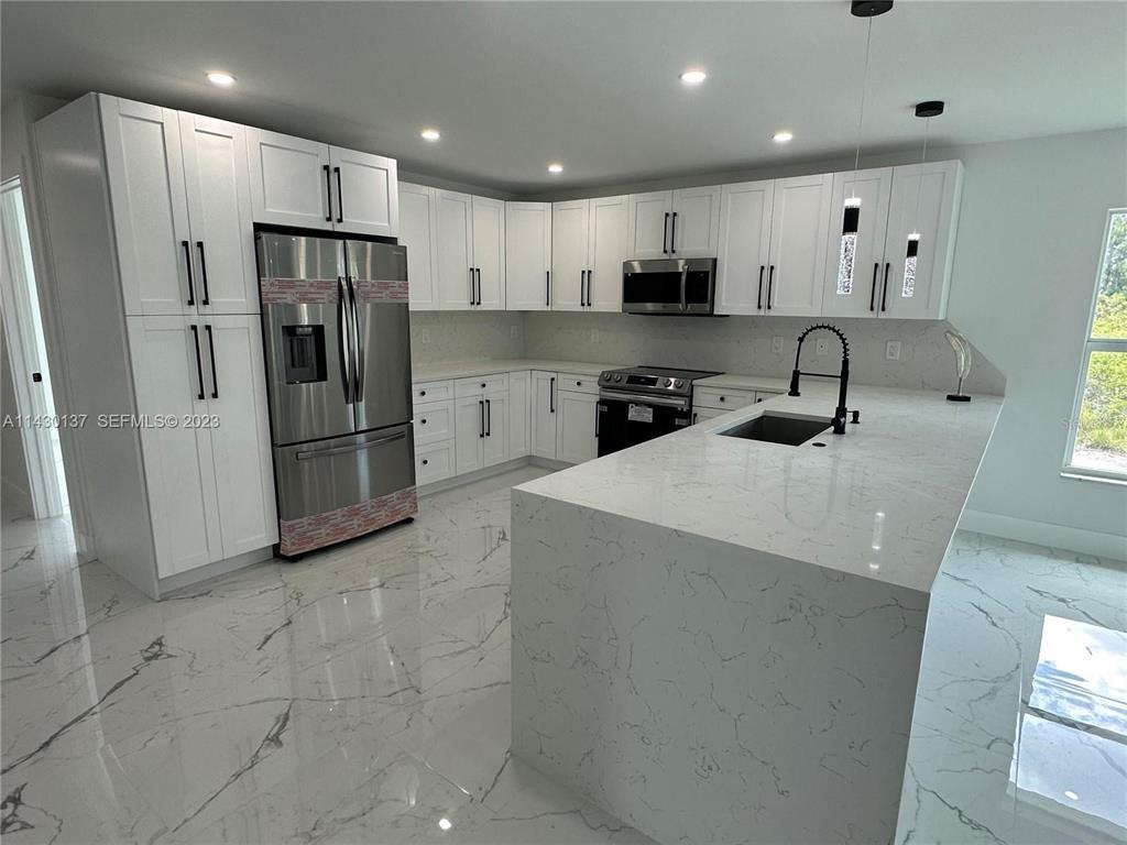 A modern kitchen features white cabinets, stainless steel appliances, and a marble-patterned island countertop — 1125 MILWAUKEE BOULEVARD, LEHIGH ACRES, FL
