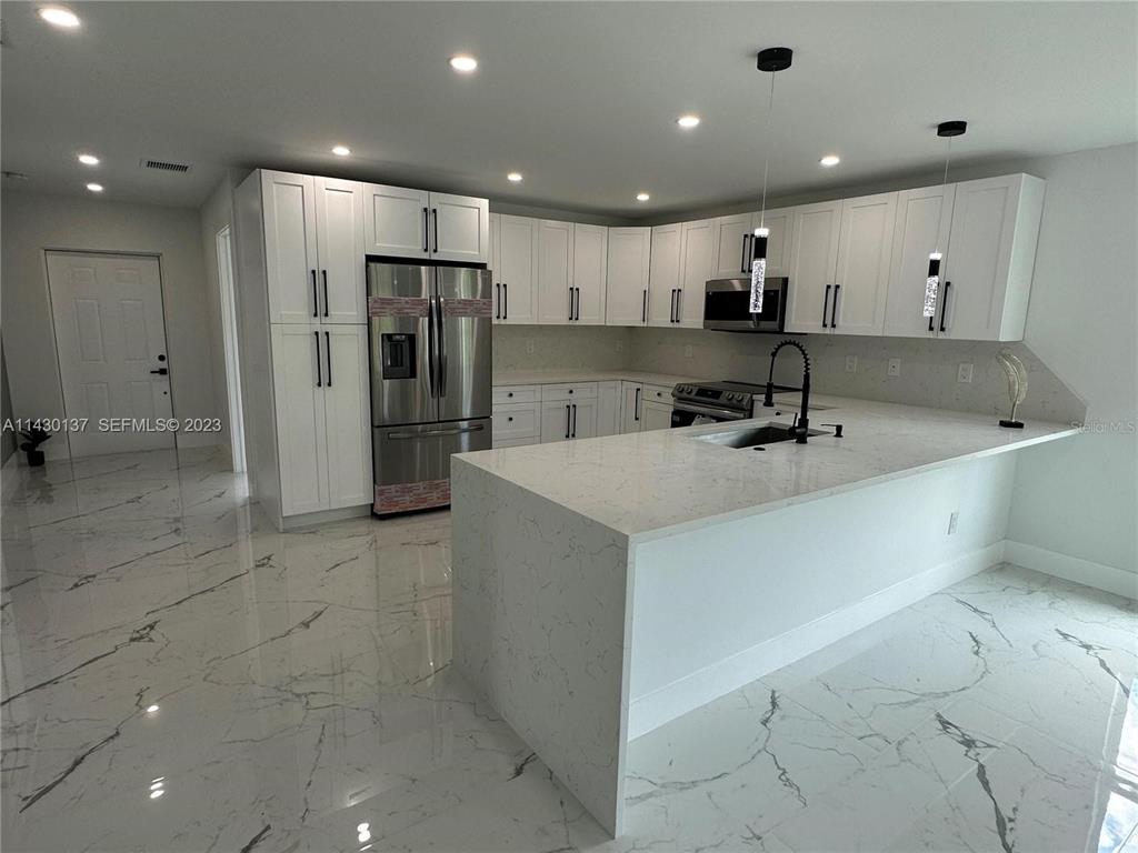 A modern kitchen features white cabinetry, stainless steel appliances, and white marble-patterned tile flooring — 1125 MILWAUKEE BOULEVARD, LEHIGH ACRES, FL