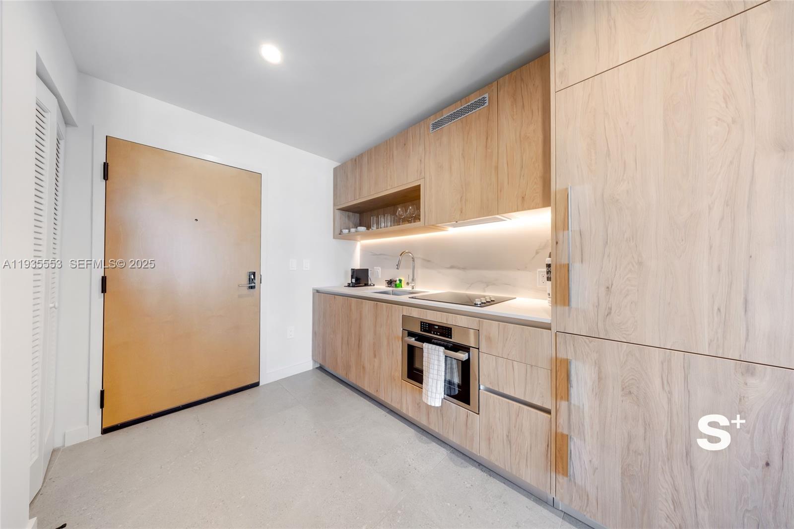 A modern kitchen features light wood cabinetry, stainless steel appliances, and a marble backsplash — 11 NE 6TH ST # 1910, Miami FL 33132, MIAMI, FL