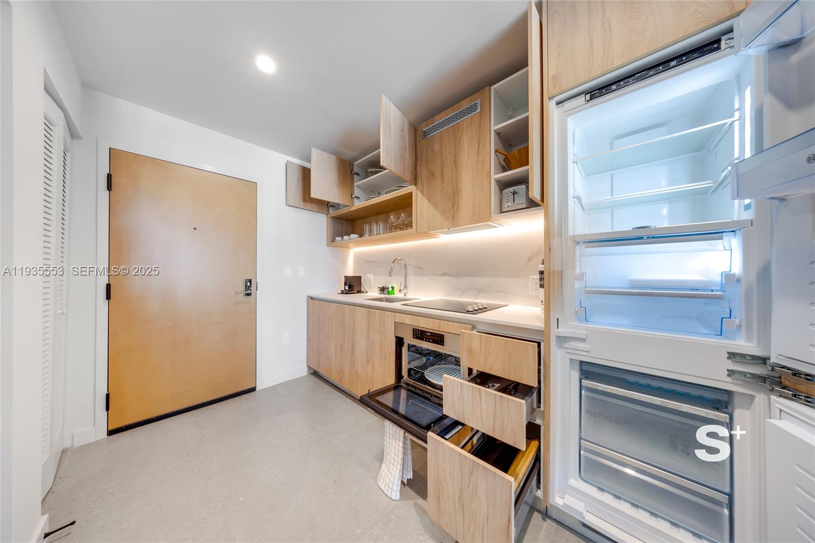 A modern kitchen features light wood cabinetry, a built-in refrigerator, and an open oven — 11 NE 6TH ST # 1910, Miami FL 33132, MIAMI, FL