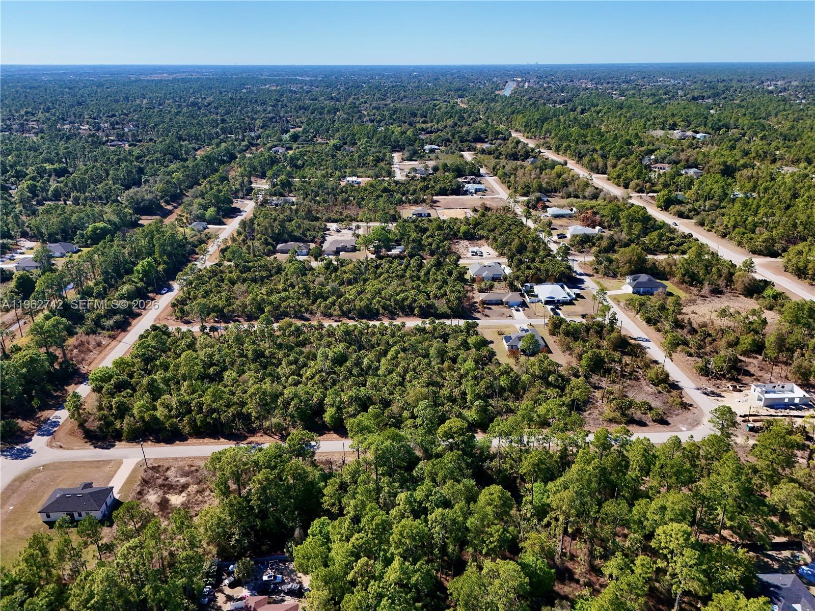 An aerial view shows a residential area with scattered houses surrounded by dense forest — 131 Navarra Ave S, Lehigh Acres FL 33974, LEHIGH ACRES, FL