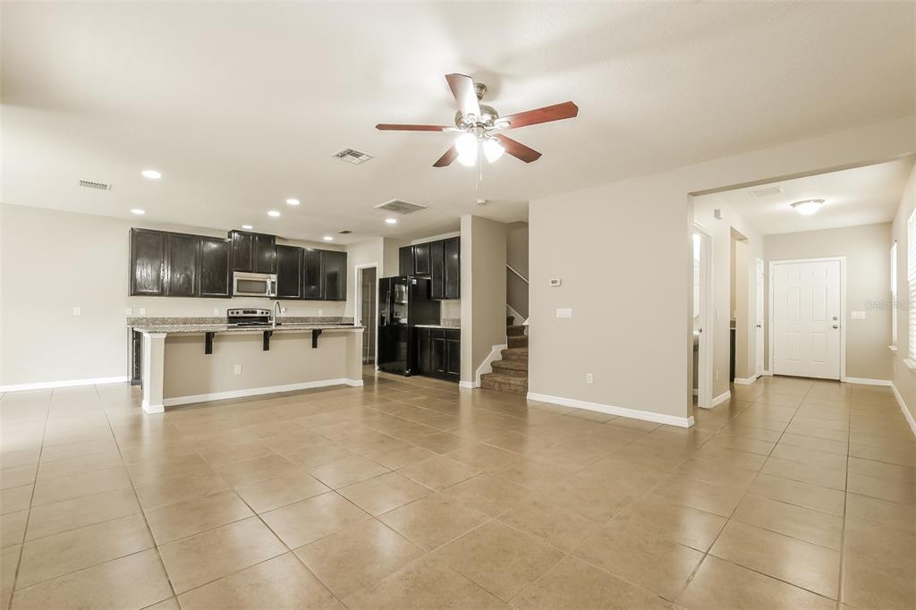 An open-concept kitchen with dark cabinets and a granite island overlooks a tiled living area — 2660 SAN SIMEON WAY, KISSIMMEE, FL