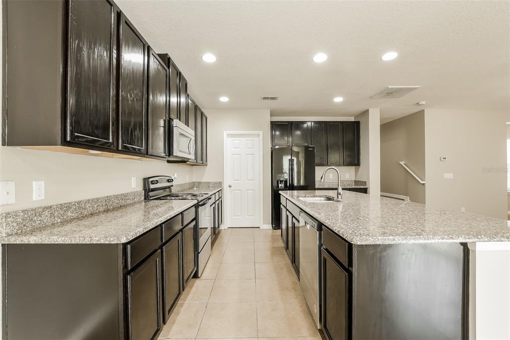 A kitchen features dark cabinets, granite countertops, a central island, and stainless steel appliances — 2660 SAN SIMEON WAY, KISSIMMEE, FL