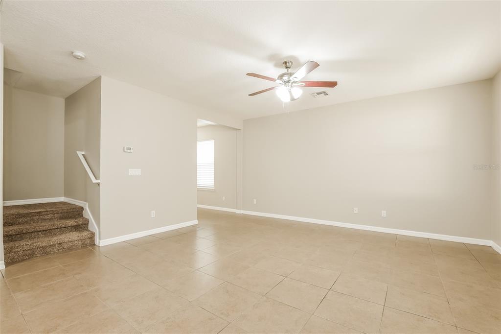 A living room with beige tile flooring, neutral walls, a ceiling fan, and carpeted stairs — 2660 SAN SIMEON WAY, KISSIMMEE, FL