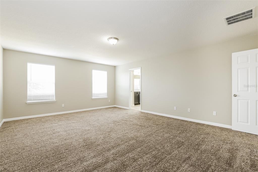 An empty bedroom with beige walls, brown carpet, two windows, and a doorway to a bathroom — 2660 SAN SIMEON WAY, KISSIMMEE, FL