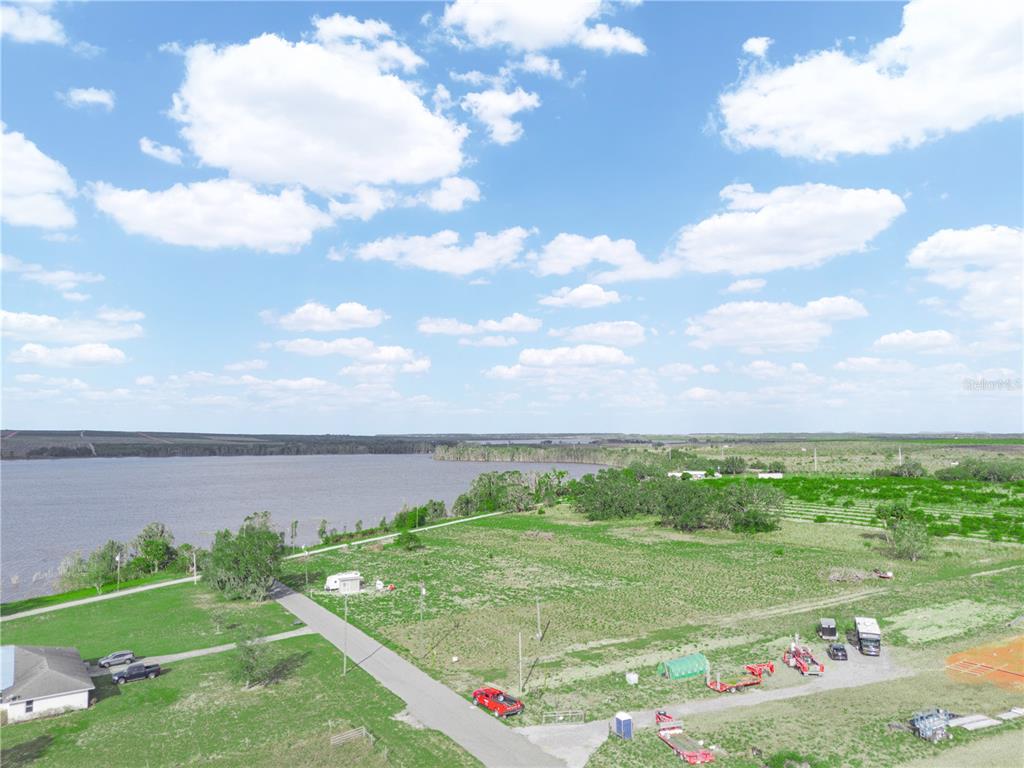 An aerial view shows a grassy lot next to a lake with a paved road — 151 EDDIE FLOOD ROAD, FROSTPROOF, FL