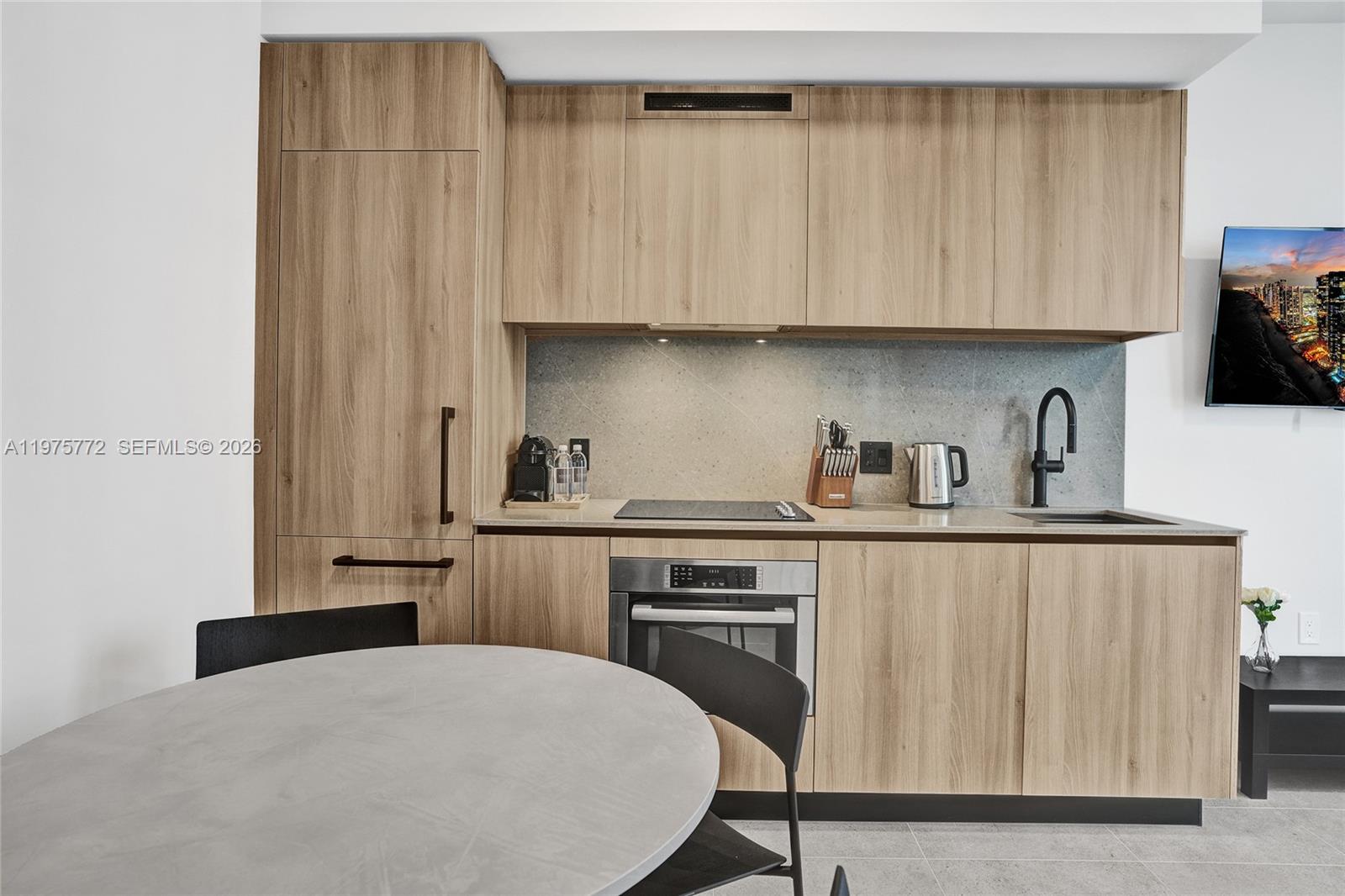A modern kitchen features light wood cabinetry, a stone backsplash, and a round dining table — 121 NE 5th St # 2411, Miami FL 33132, MIAMI, FL