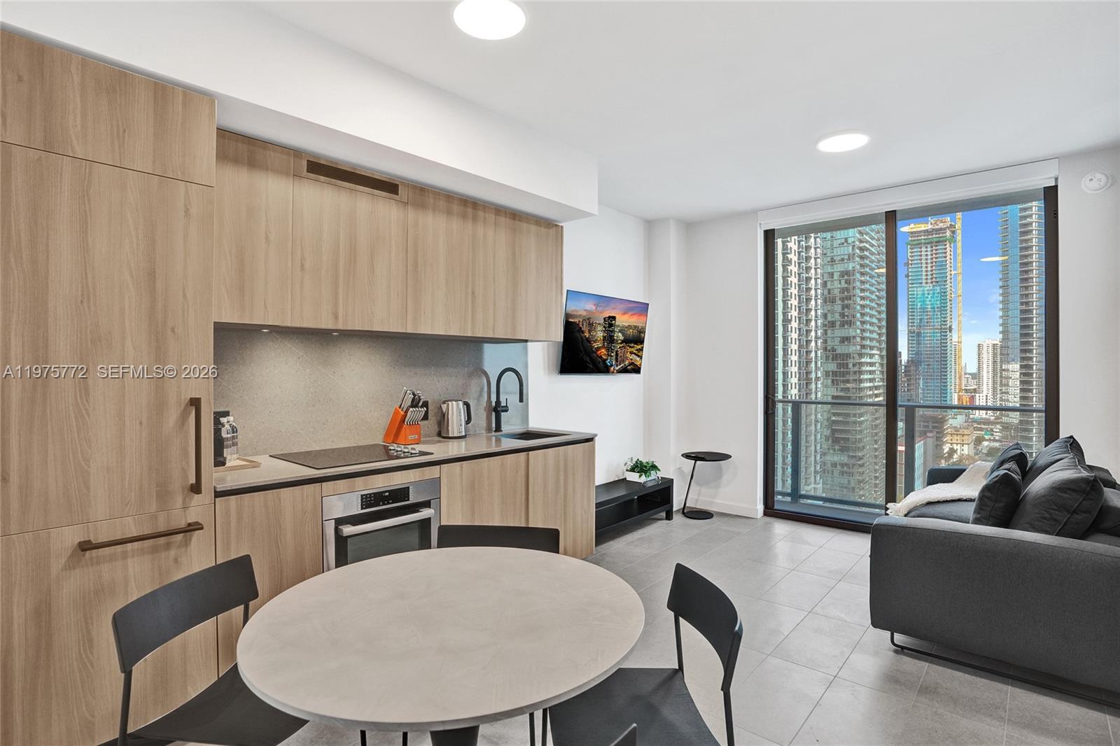 A modern studio apartment features a kitchenette with wood cabinetry and a city view — 121 NE 5th St # 2411, Miami FL 33132, MIAMI, FL