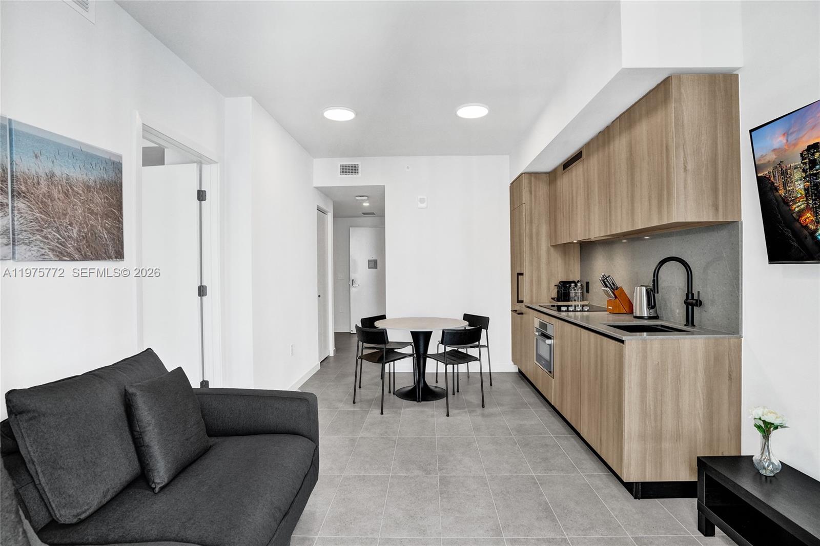 A modern studio apartment features a kitchenette, dining area, and a dark gray sofa — 121 NE 5th St # 2411, Miami FL 33132, MIAMI, FL
