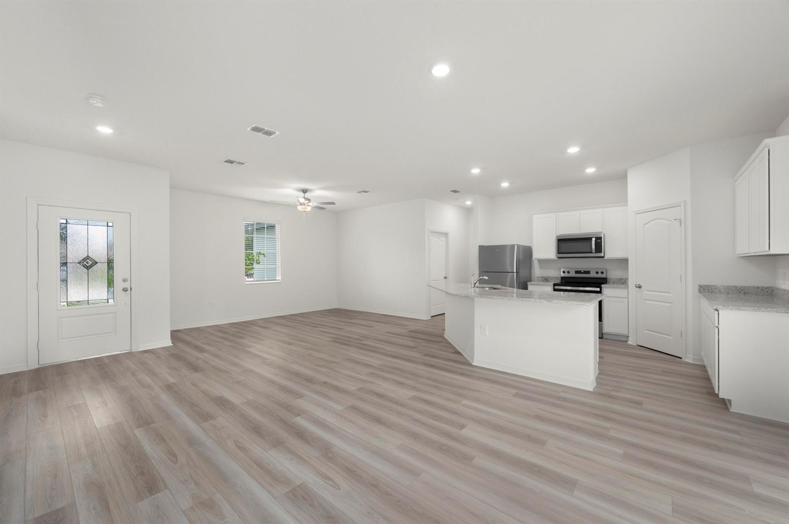 An open-concept living area features light wood-look flooring, white walls, and a modern kitchen — 9375 103rd Avenue, Vero Beach FL 32967, VERO BEACH, FL