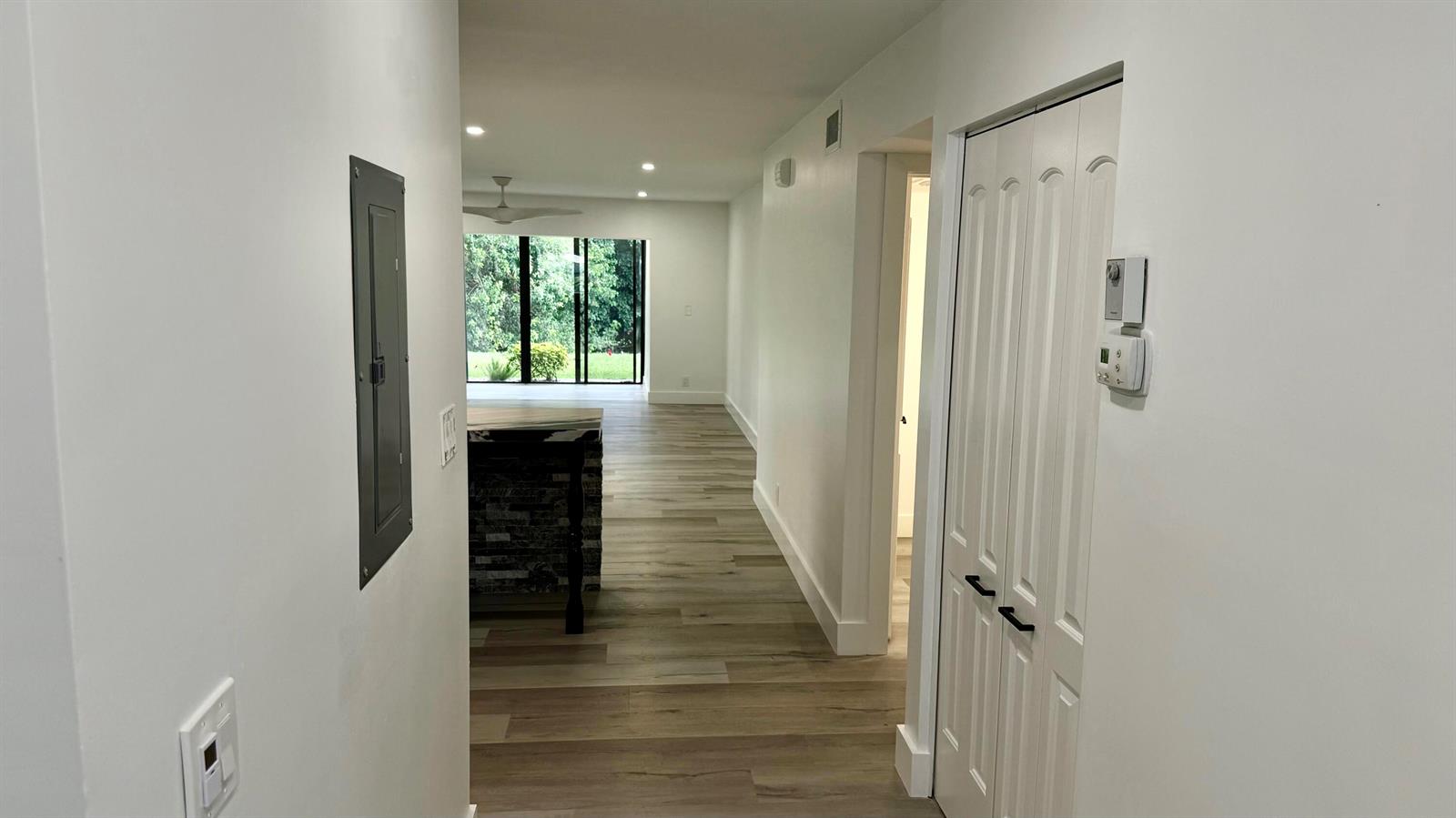 A hallway with wood-look flooring leads to a living area with a sliding glass door — 21695 Tall Palm Circle # 4a, Boca Raton FL 33433, BOCA RATON, FL