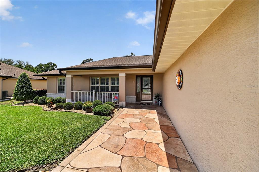 A stone-paved walkway leads to the front entrance of a house with a tan exterior — 16364 SE 89TH TERRACE, SUMMERFIELD, FL