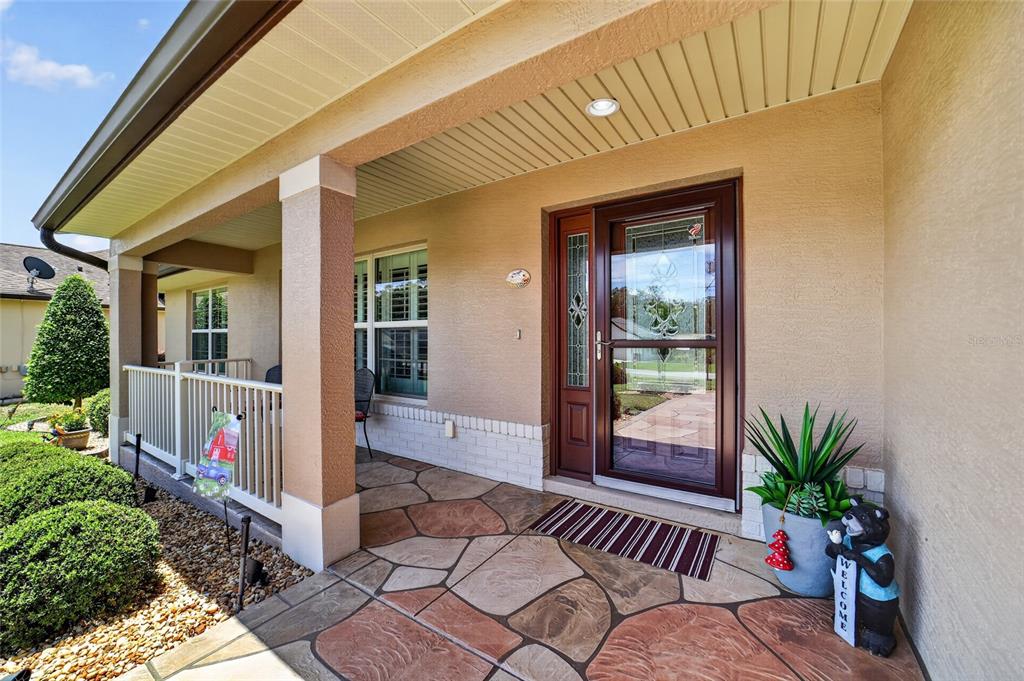 A covered front porch features stone-patterned flooring, a brown storm door, and a white railing — 16364 SE 89TH TERRACE, SUMMERFIELD, FL