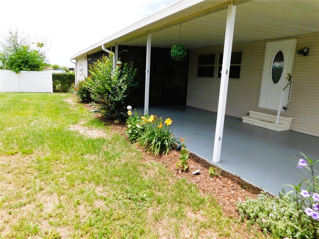 A covered concrete patio sits beside a house with a lawn and garden bed — 5315 ANTIGUA DRIVE, ZEPHYRHILLS, FL