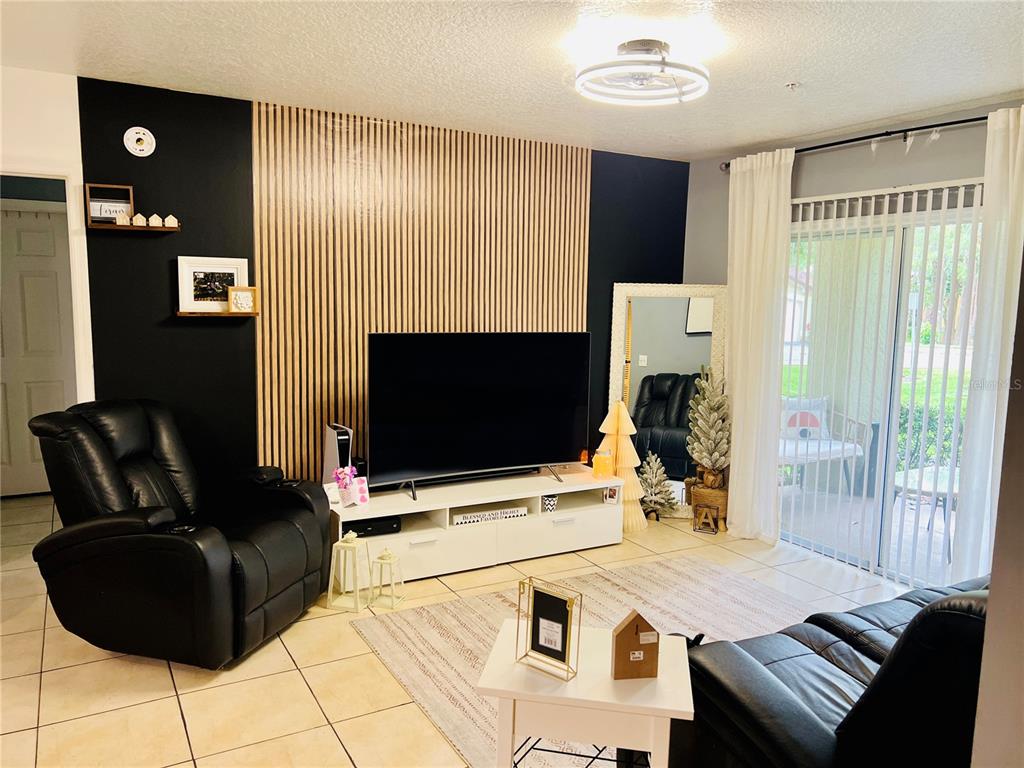 A living room features a black accent wall with wood slats, a television, and furniture — 737 CREST PINES DRIVE UNIT 612, ORLANDO, FL