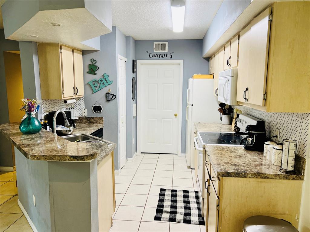A kitchen features light wood cabinets, granite-look countertops, white appliances, and a tiled floor — 737 CREST PINES DRIVE UNIT 612, ORLANDO, FL