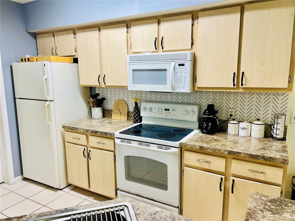 A kitchen features light wood cabinets, a white stove, a microwave, and a herringbone backsplash — 737 CREST PINES DRIVE UNIT 612, ORLANDO, FL