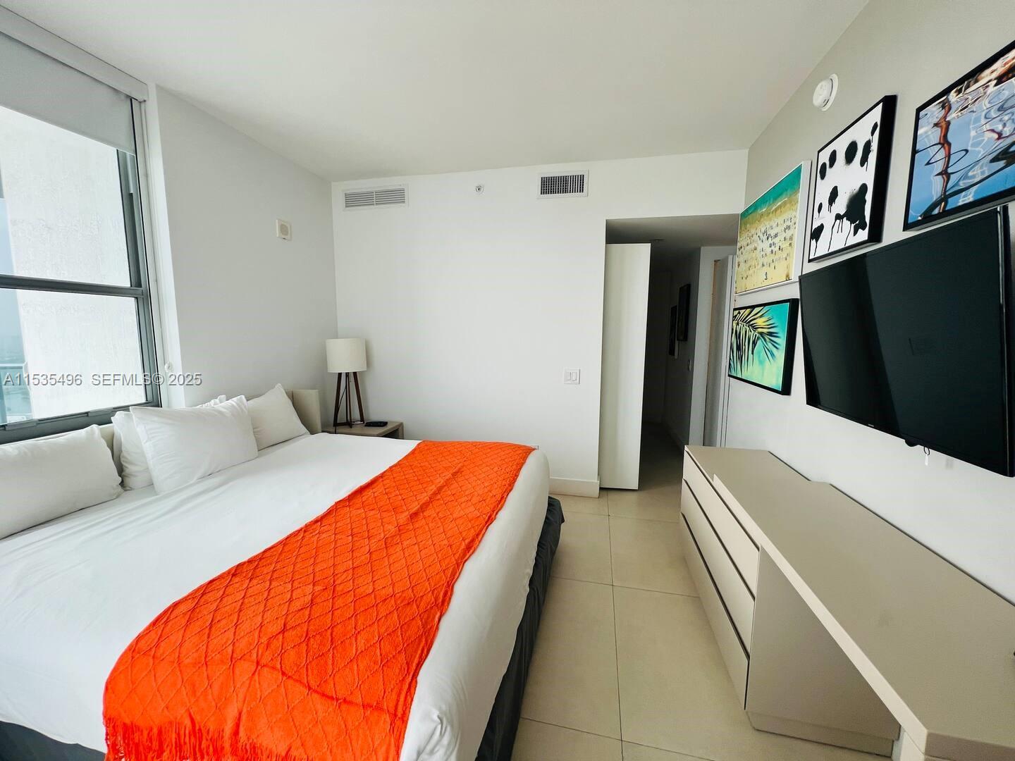 A bedroom features a bed with an orange runner, a wall-mounted television, and tiled flooring — 4111 S Ocean Dr # 2611, Hollywood FL 33019, HOLLYWOOD, FL