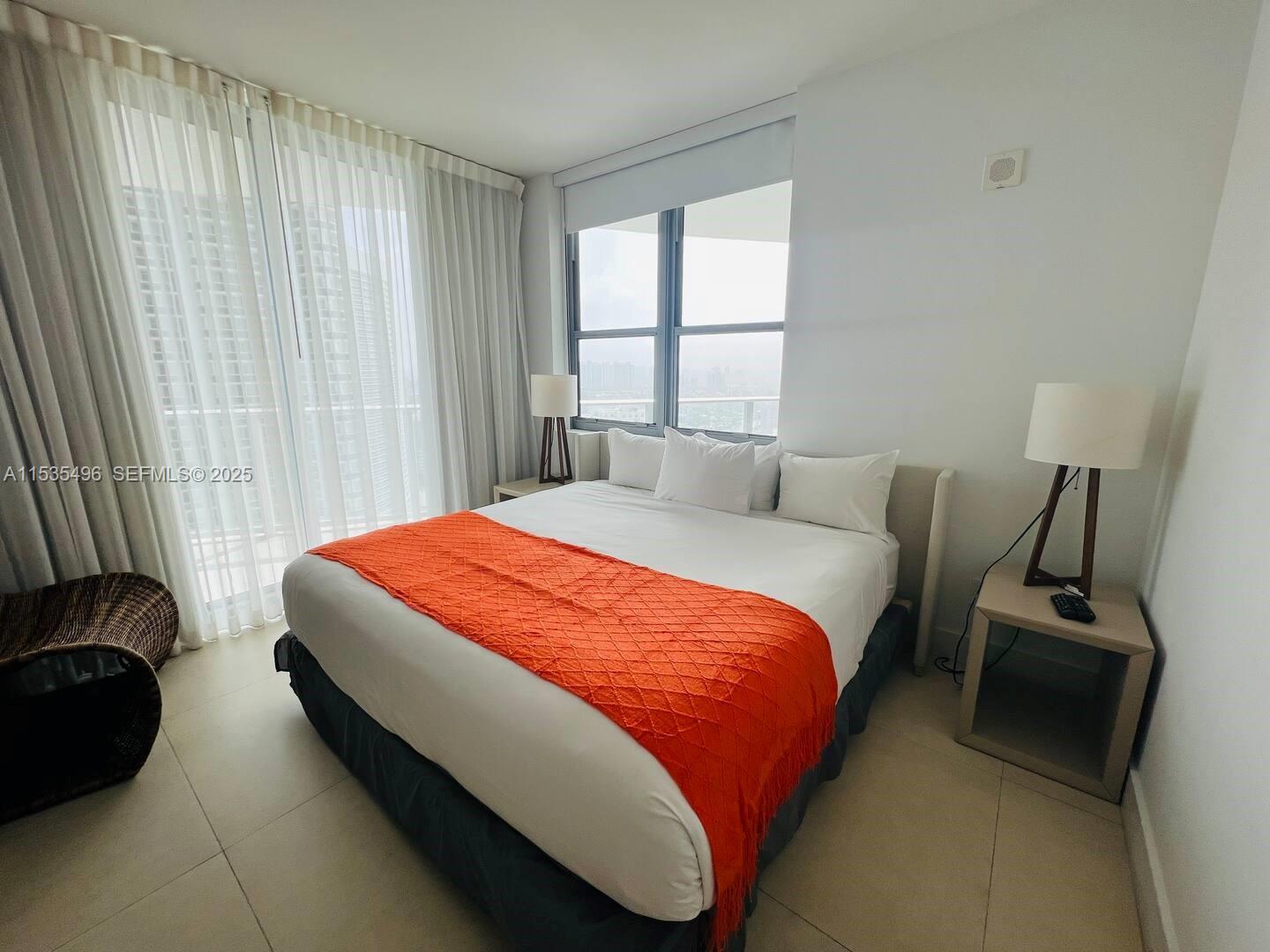 A bedroom features a bed with an orange throw, bedside tables, and floor-to-ceiling curtains — 4111 S Ocean Dr # 2611, Hollywood FL 33019, HOLLYWOOD, FL