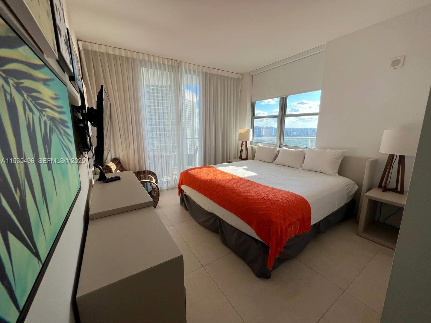 A bedroom features a king bed with an orange throw, tile floors, and floor-to-ceiling curtains — 4111 S Ocean Dr # 2611, Hollywood FL 33019, HOLLYWOOD, FL