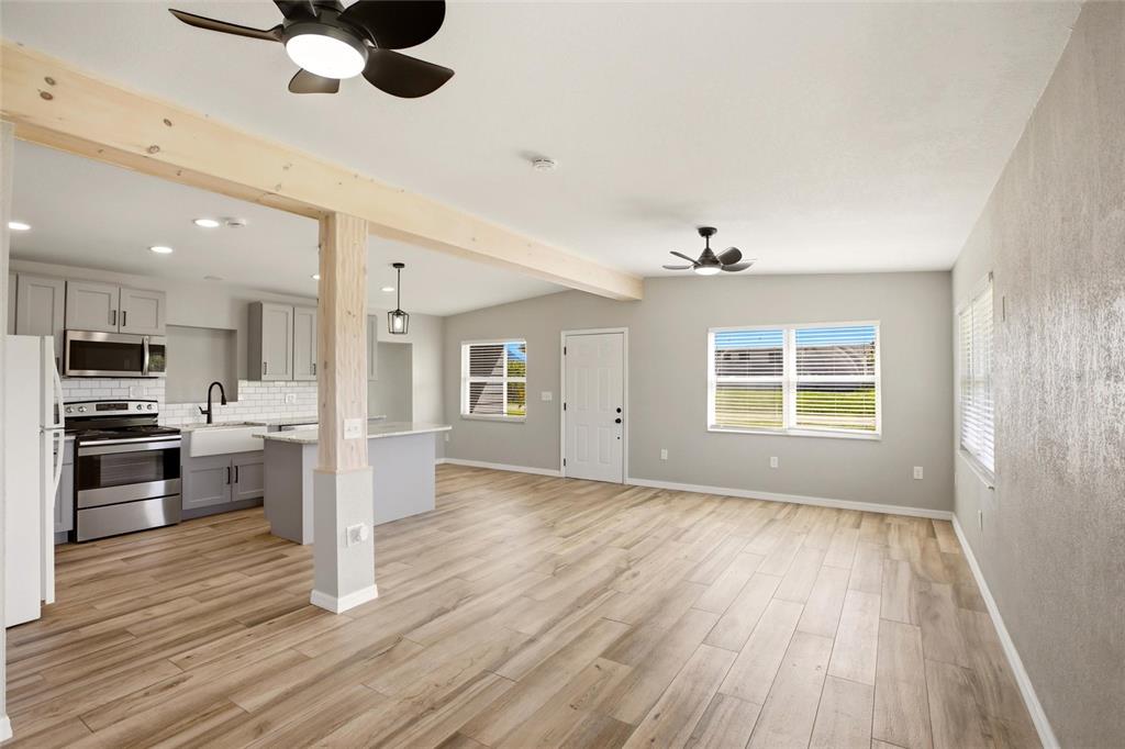 An open-concept kitchen and living area featuring light wood-look flooring and a wooden support beam — 3927 VASCO STREET, PUNTA GORDA, FL