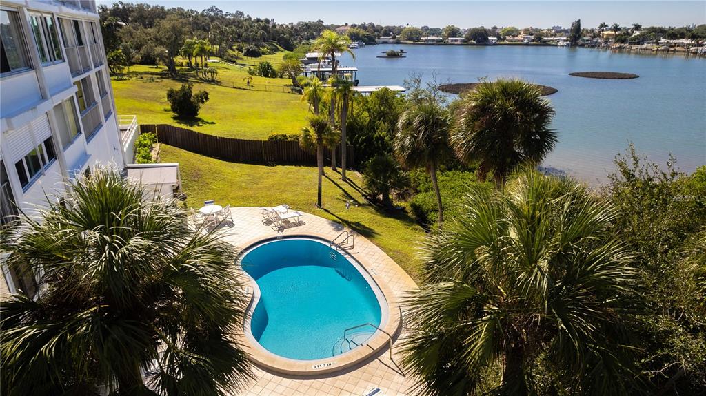An elevated view of a kidney-shaped swimming pool next to a building overlooking a lake — 50 HARBOR VIEW LANE UNIT 11, BELLEAIR BLUFFS, FL