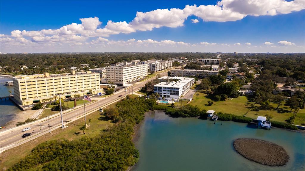 An aerial view shows multi-story apartment buildings situated along a road near a coastal inlet — 50 HARBOR VIEW LANE UNIT 11, BELLEAIR BLUFFS, FL
