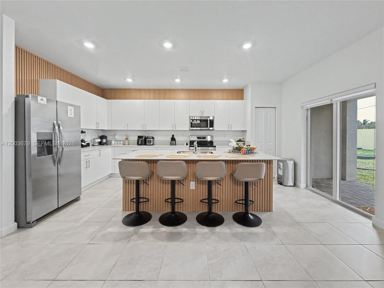 A modern kitchen features white cabinetry, a wood-slatted island, and stainless steel appliances — 13218 SW 189th Ter, Miami FL 33177, MIAMI, FL