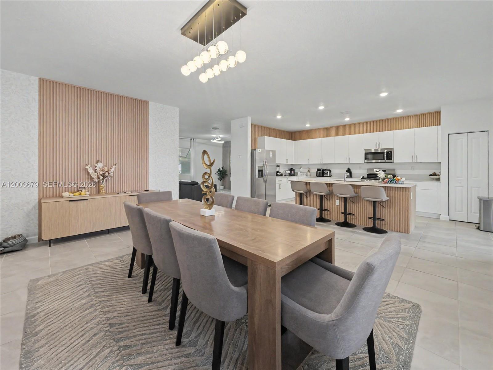 A dining area with a wooden table and grey chairs sits before an open kitchen — 13218 SW 189th Ter, Miami FL 33177, MIAMI, FL