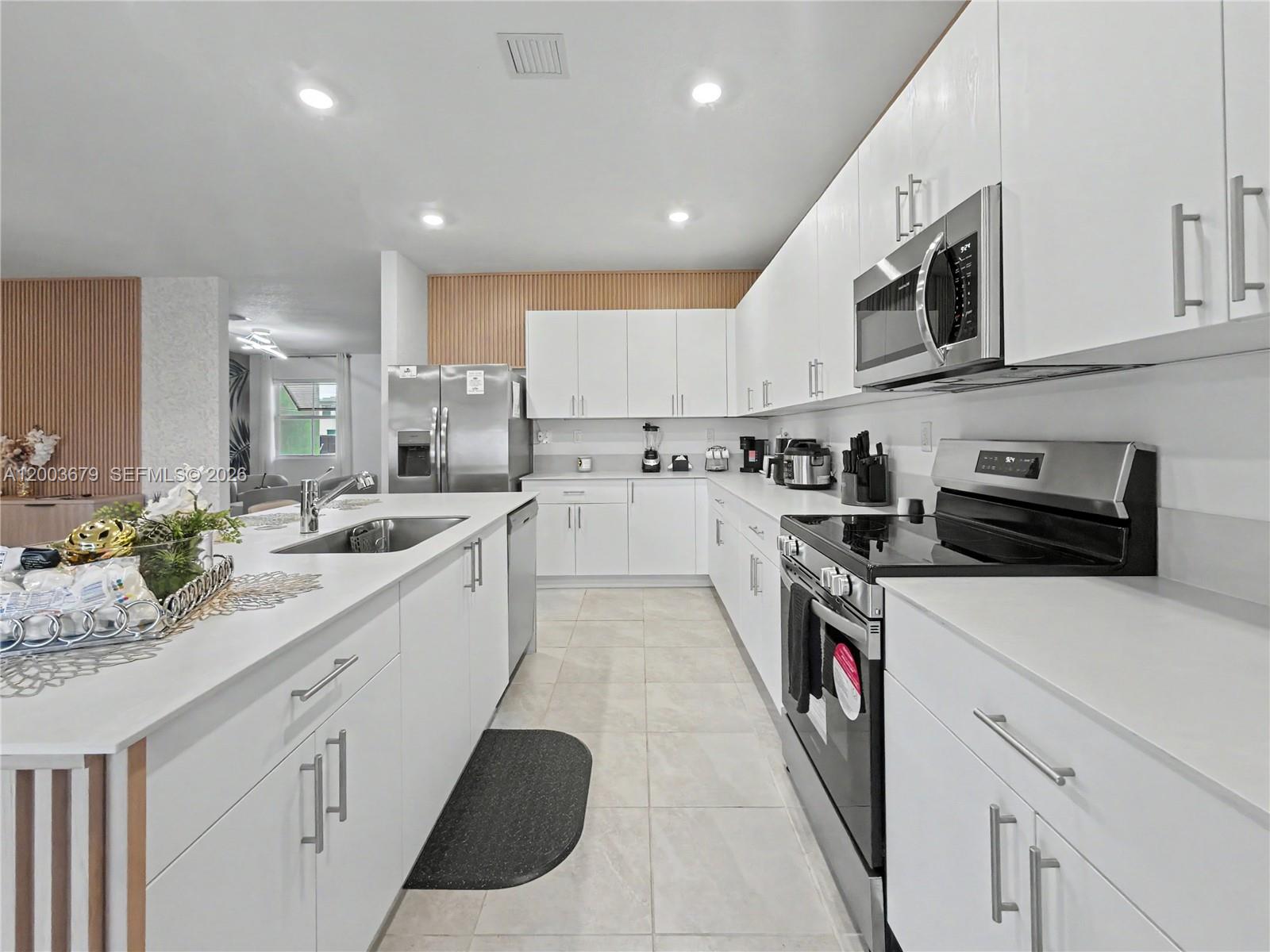 A modern kitchen features white cabinetry, stainless steel appliances, and a large central island — 13218 SW 189th Ter, Miami FL 33177, MIAMI, FL