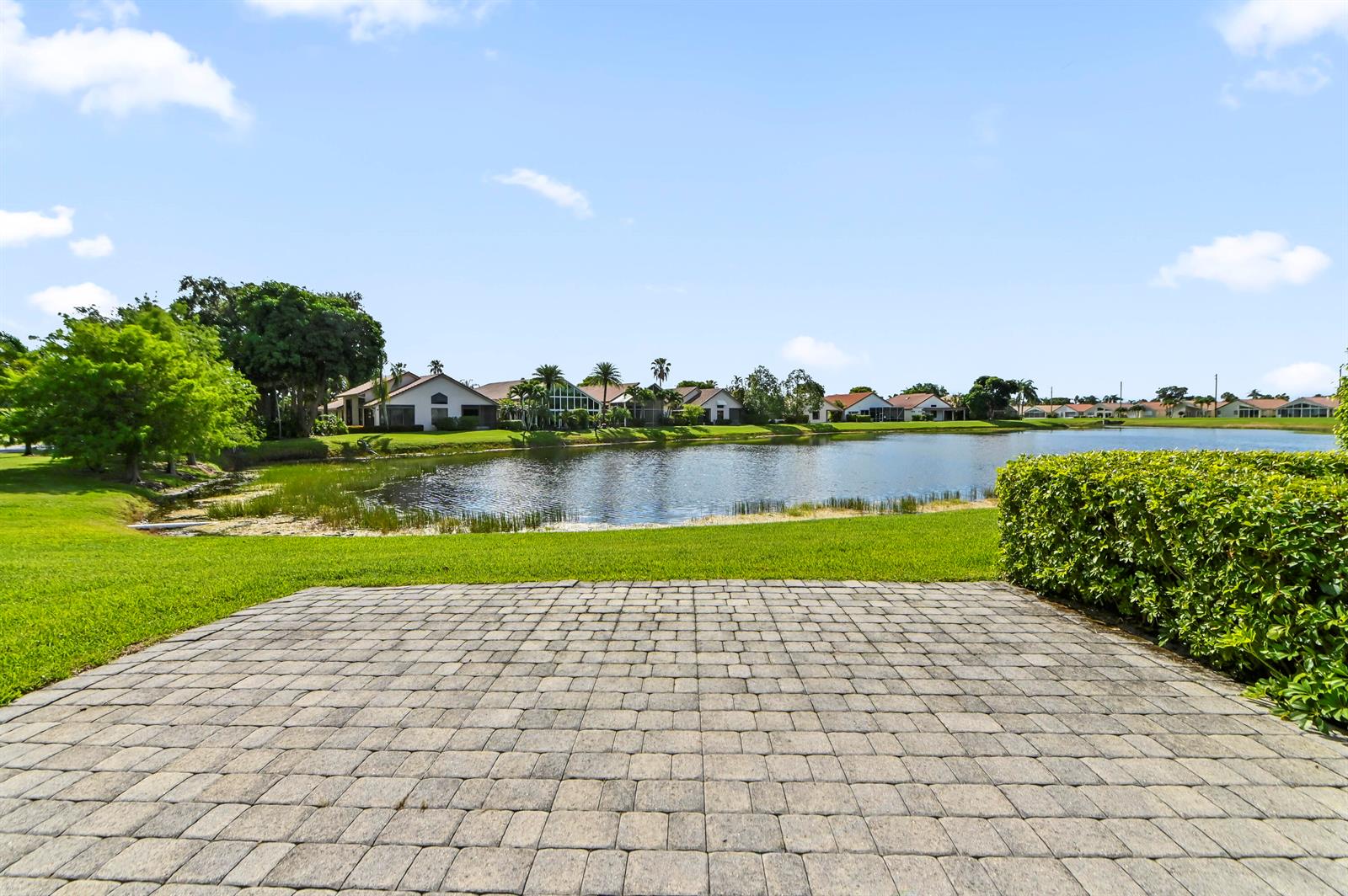 A paved patio overlooks a lake surrounded by houses and green landscaping under a blue sky — 6226 Water Lilly Lane, Boynton Beach FL 33437, BOYNTON BEACH, FL