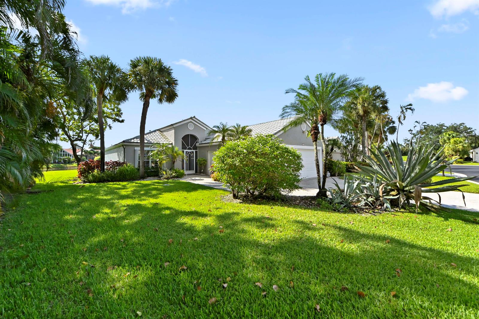 A single-story house with a white garage and palm trees sits on a green lawn — 6226 Water Lilly Lane, Boynton Beach FL 33437, BOYNTON BEACH, FL