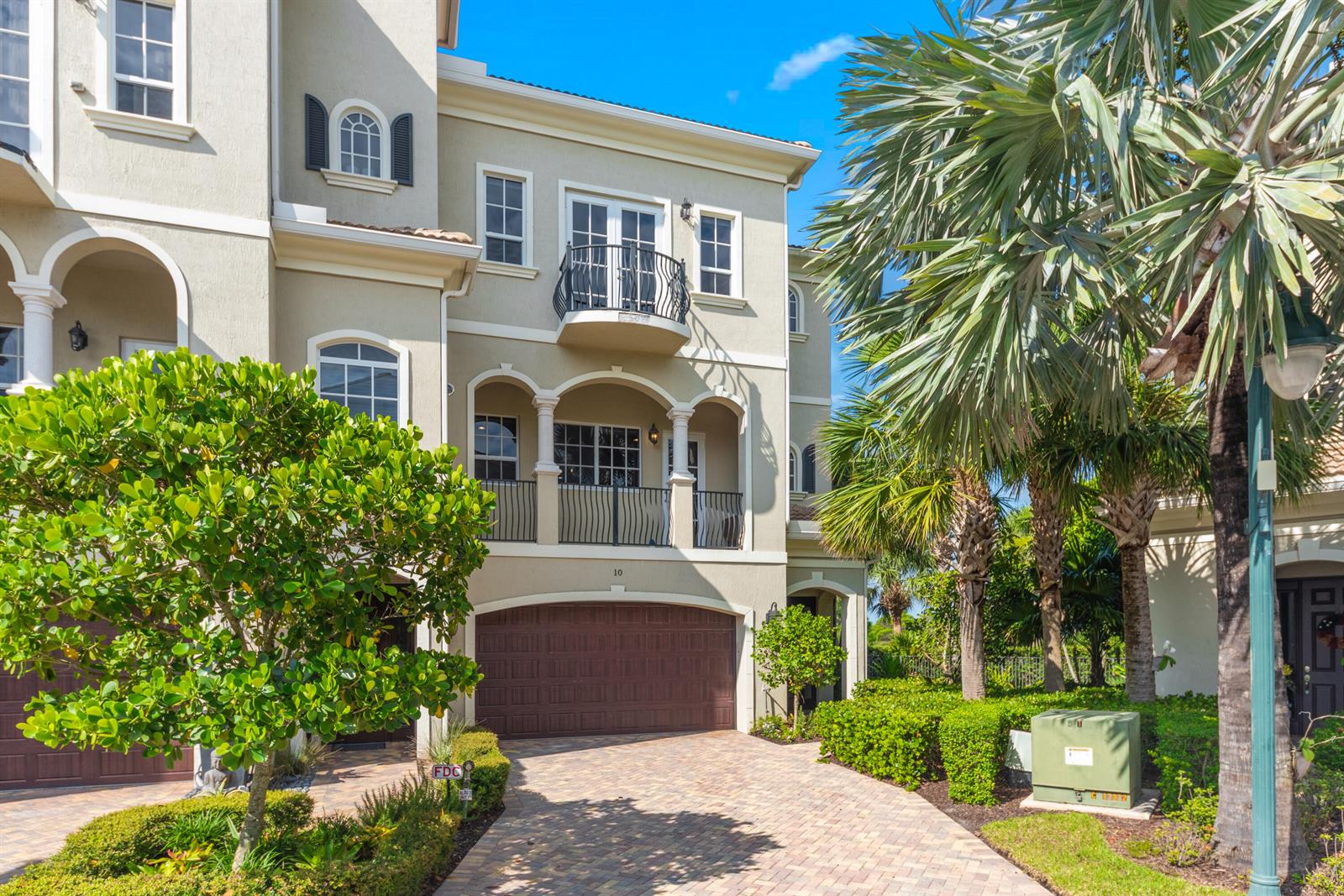 A three-story townhouse with a brown garage door, a balcony, and a paved driveway — 144 Tierra Lane # 10, Jupiter FL 33477, JUPITER, FL