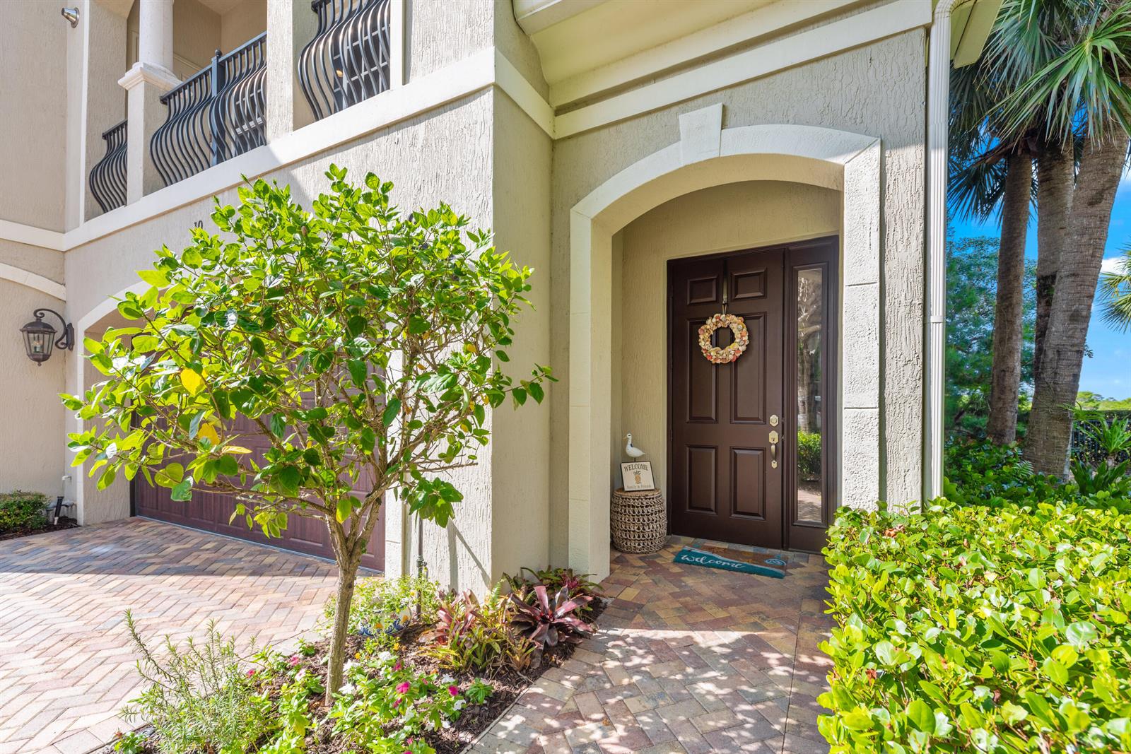 The exterior of a house features a brown front door, a brick driveway, and landscaping — 144 Tierra Lane # 10, Jupiter FL 33477, JUPITER, FL