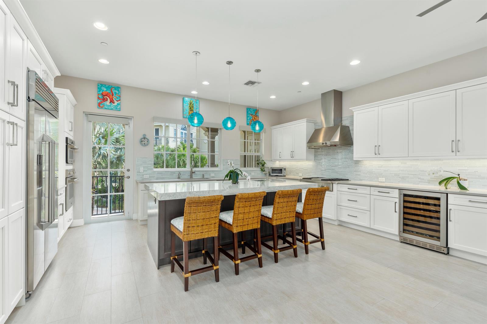 A modern kitchen features white cabinetry, a dark island with wicker stools, and blue pendants — 144 Tierra Lane # 10, Jupiter FL 33477, JUPITER, FL
