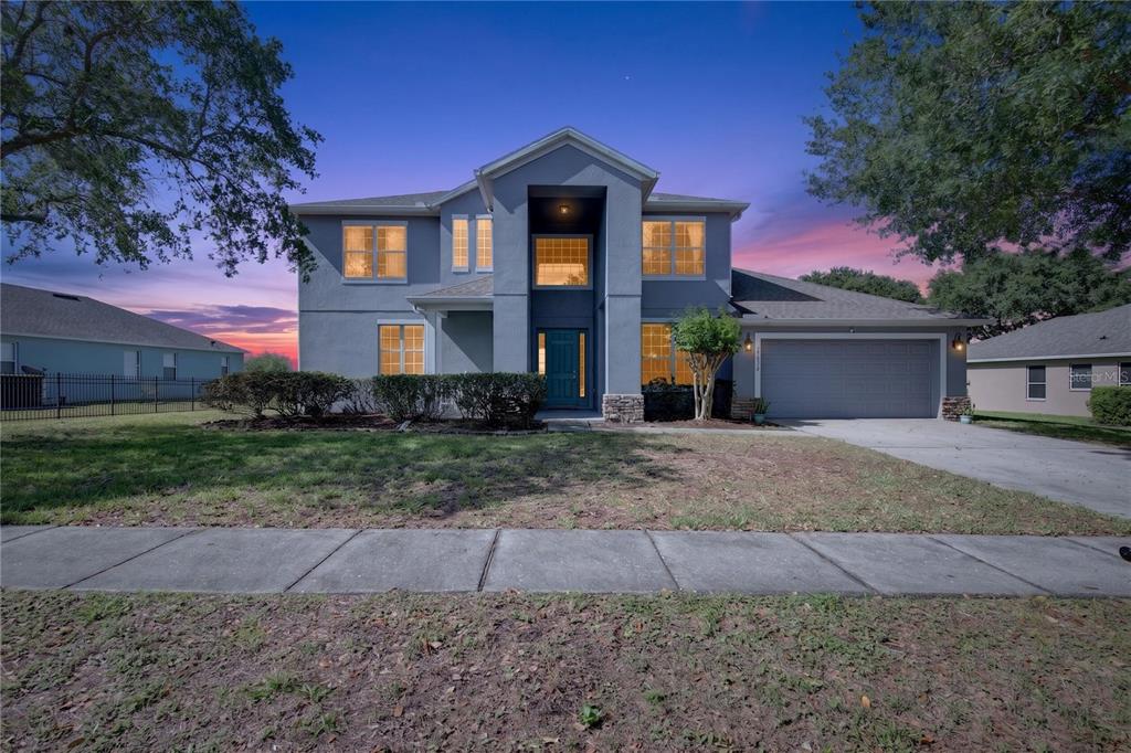 A two-story gray house with a two-car garage and a teal front door at dusk — 23626 VALDERAMA LANE, SORRENTO, FL