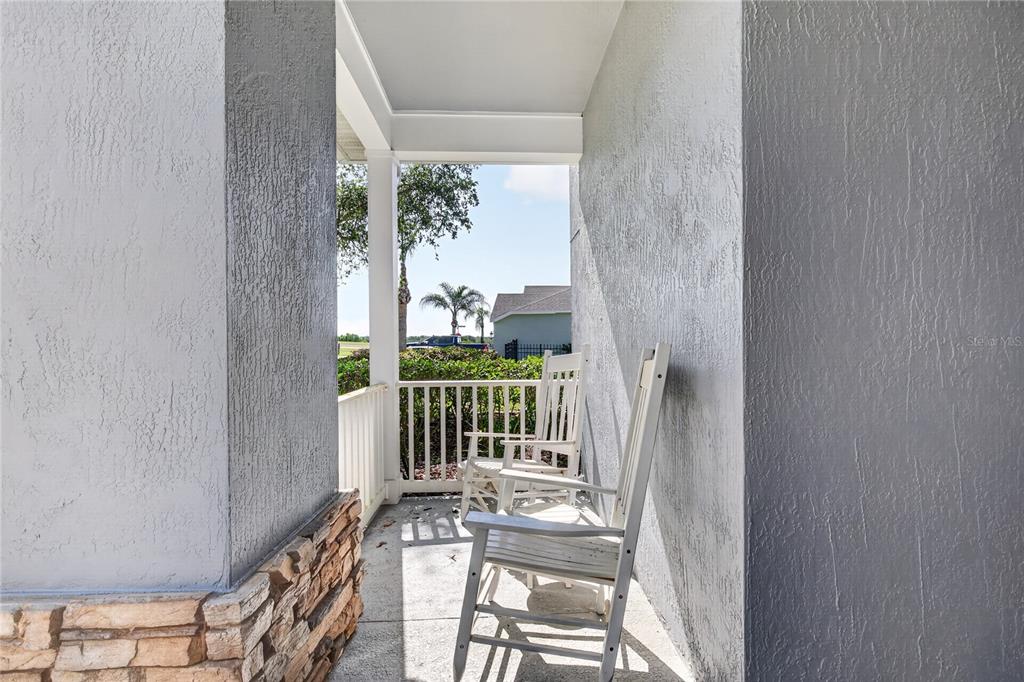 A covered front porch features two white rocking chairs and stone veneer accents — 23626 VALDERAMA LANE, SORRENTO, FL