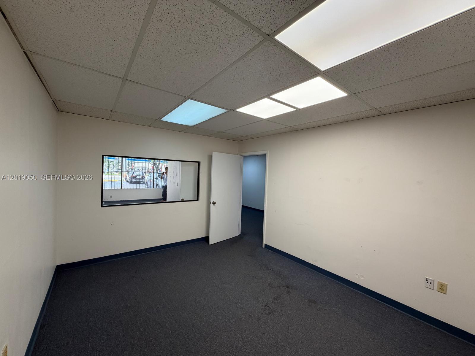 An empty office room features gray carpeting, white walls, a window, and a doorway — 2501 NW 72nd Ave # B, Miami FL 33122, MIAMI, FL
