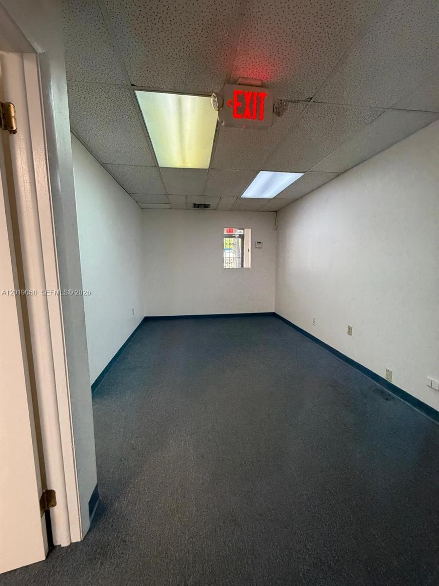 An empty office room features a drop ceiling, blue carpeting, and a small window — 2501 NW 72nd Ave # B, Miami FL 33122, MIAMI, FL